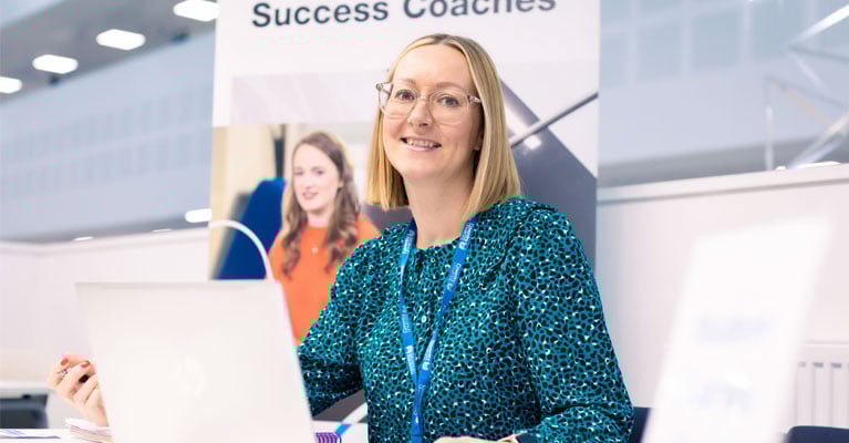 A success coach with an open laptop in front of her, smiling at the camera.