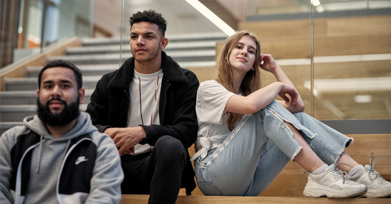 A group of students sitting together on stairs with a glass bannister.