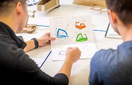 two male students looking at colourful product designs on a design sheet