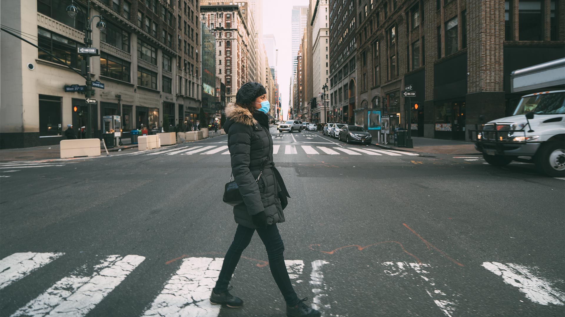 A woman crossing a wide New York street wearing a mask 