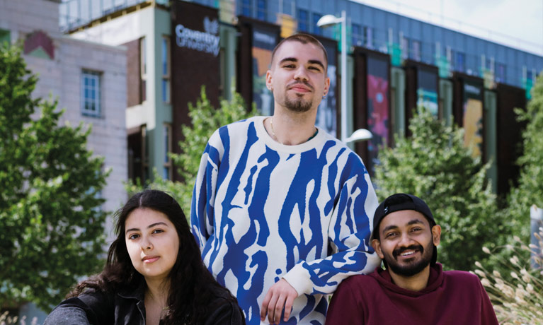 Three students posing outside a campus building with greenery in the background