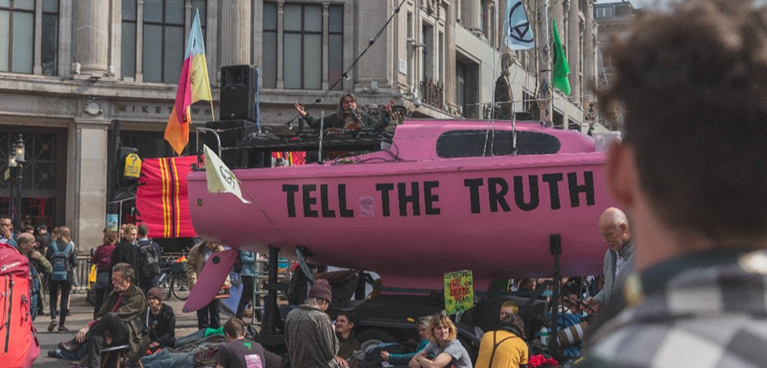 A pink sign reading tell the truth surrounded by people
