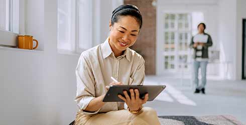 Asian lady sitting on a bench looking at tablet
