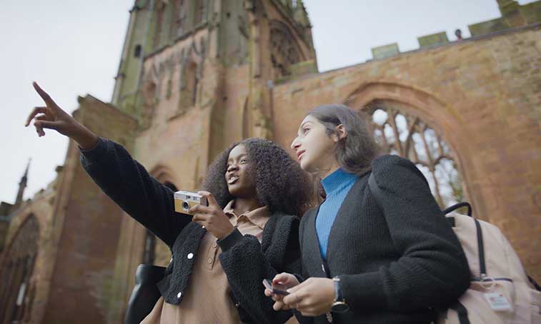 Two students in the cathedral ruins, one pointing up at something.
