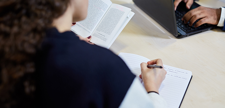 Woman writing in a notebook and man working at a laptop