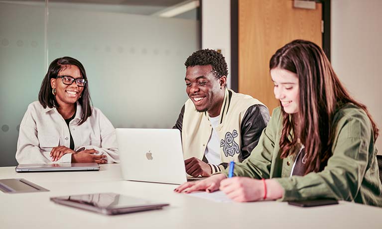 Three students sat in a room looking at a laptop