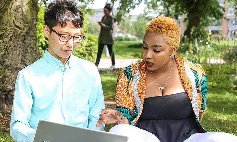 Two students sat outside on the grass